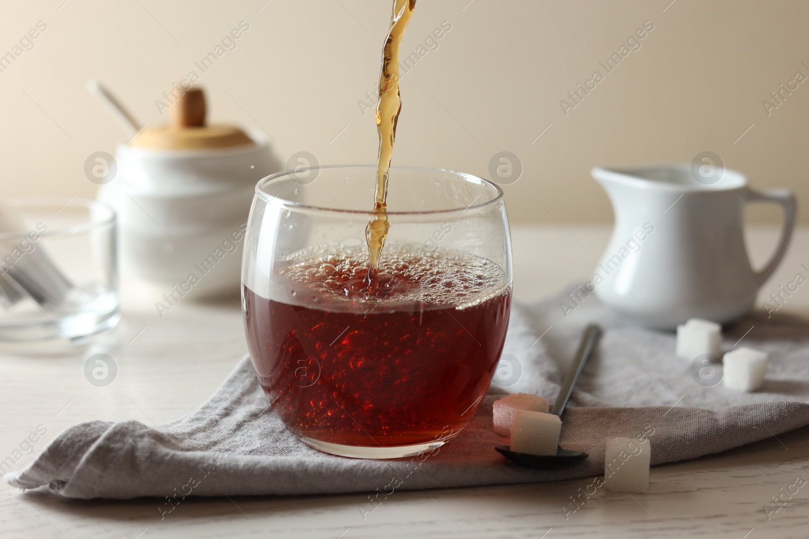 Photo of Pouring warm tea into cup on white wooden table, closeup