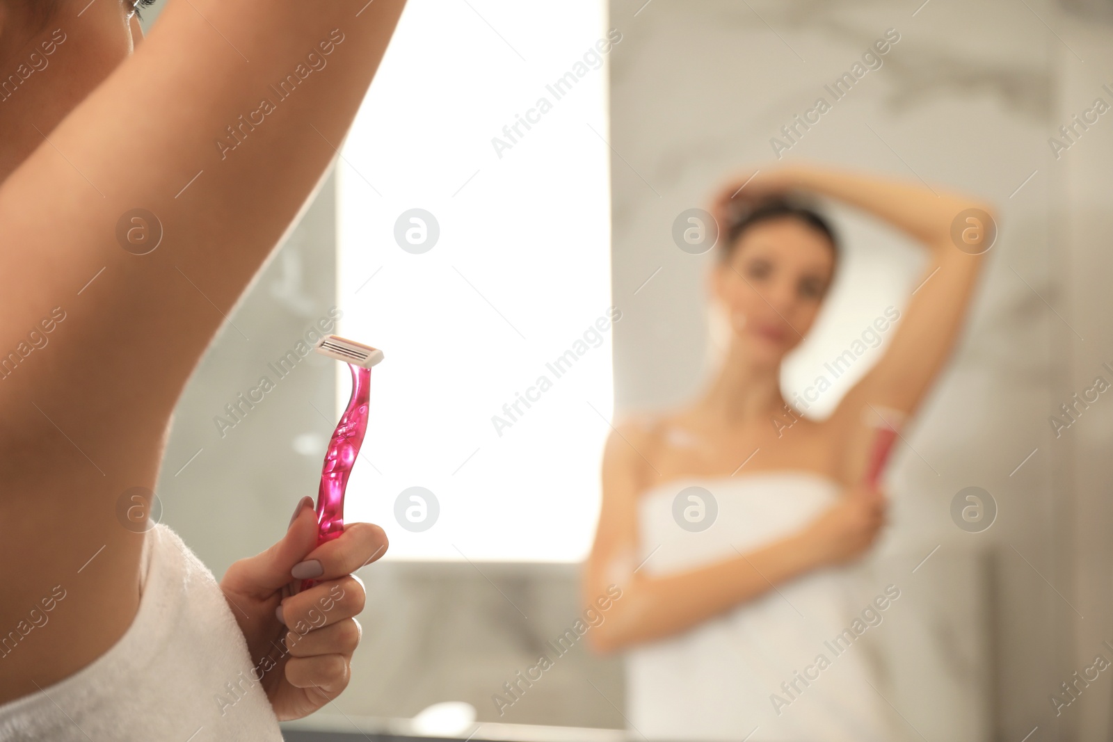 Photo of Young woman shaving armpit in bathroom, closeup