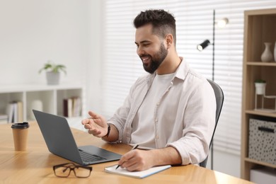 Young man using video chat during webinar at table in room