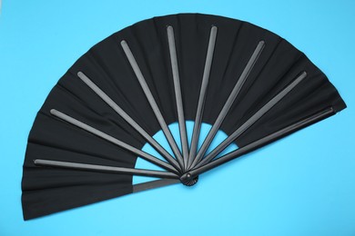 Stylish black hand fan on light blue background, top view