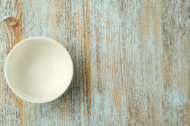 Photo of Stylish empty ceramic bowl on light blue wooden table, top view and space for text. Cooking utensil