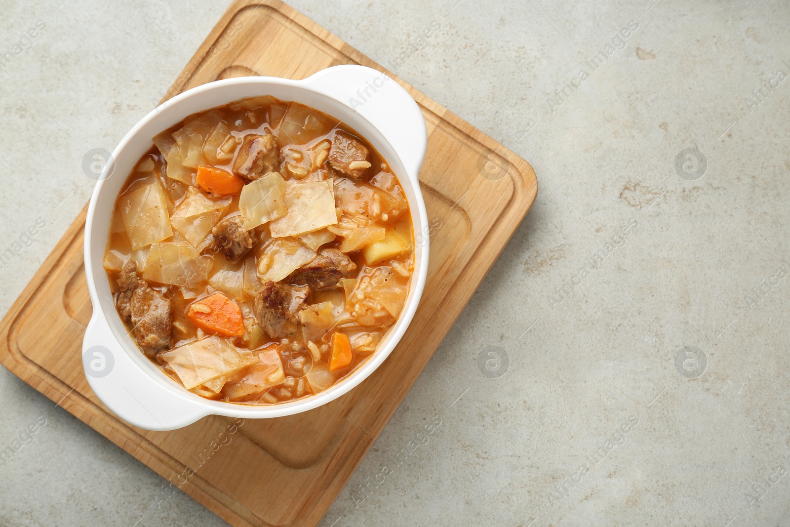 Photo of Tasty cabbage soup with meat and carrot on light grey textured table, top view. Space for text