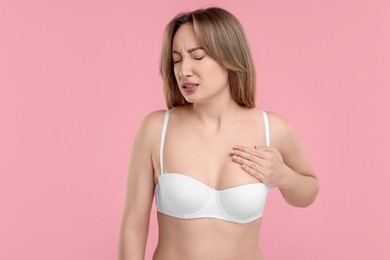 Mammology. Young woman doing breast self-examination on pink background