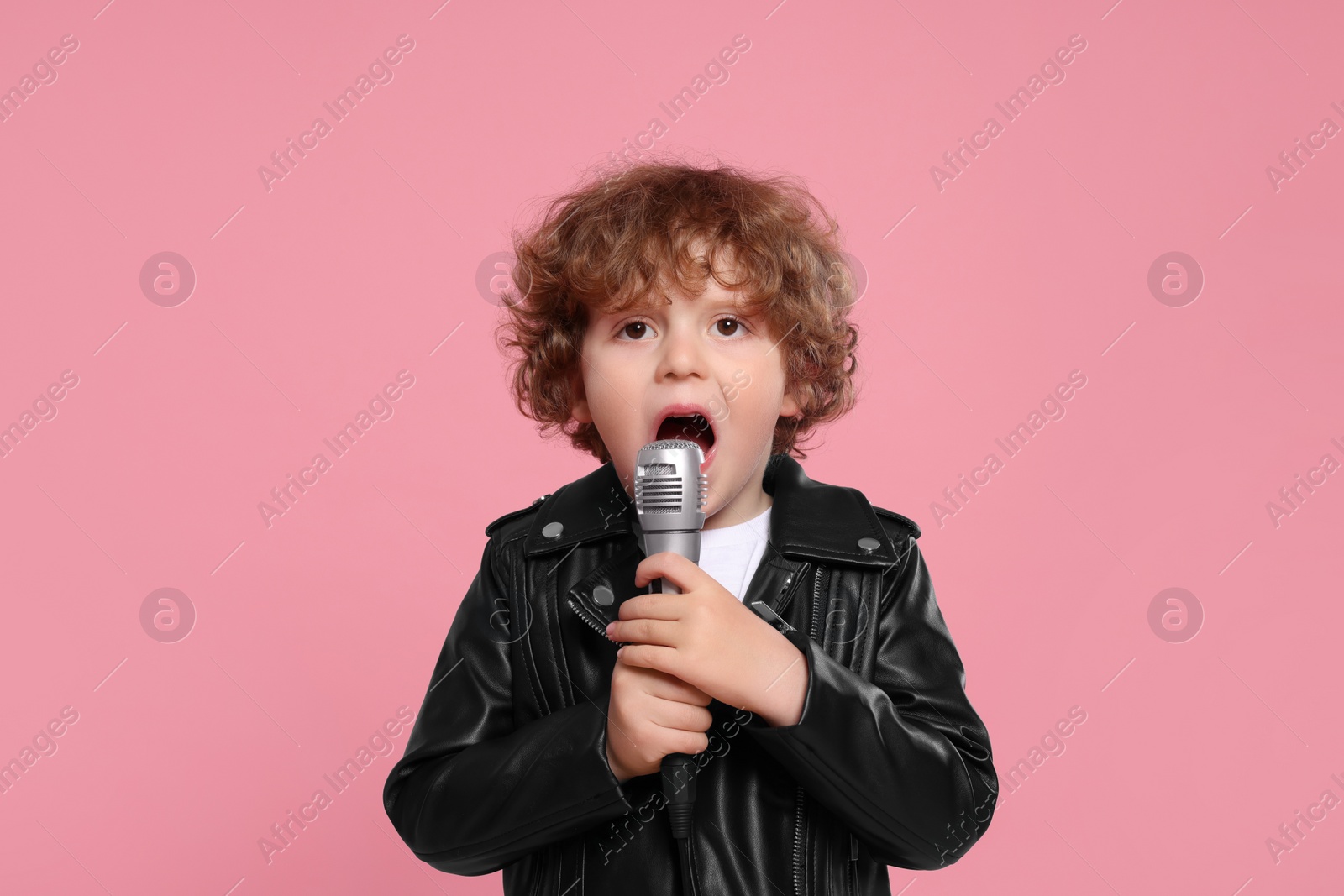 Photo of Cute little boy with microphone singing on pink background