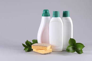 Photo of Bottles of cleaning product, sponges and green leaves on light background