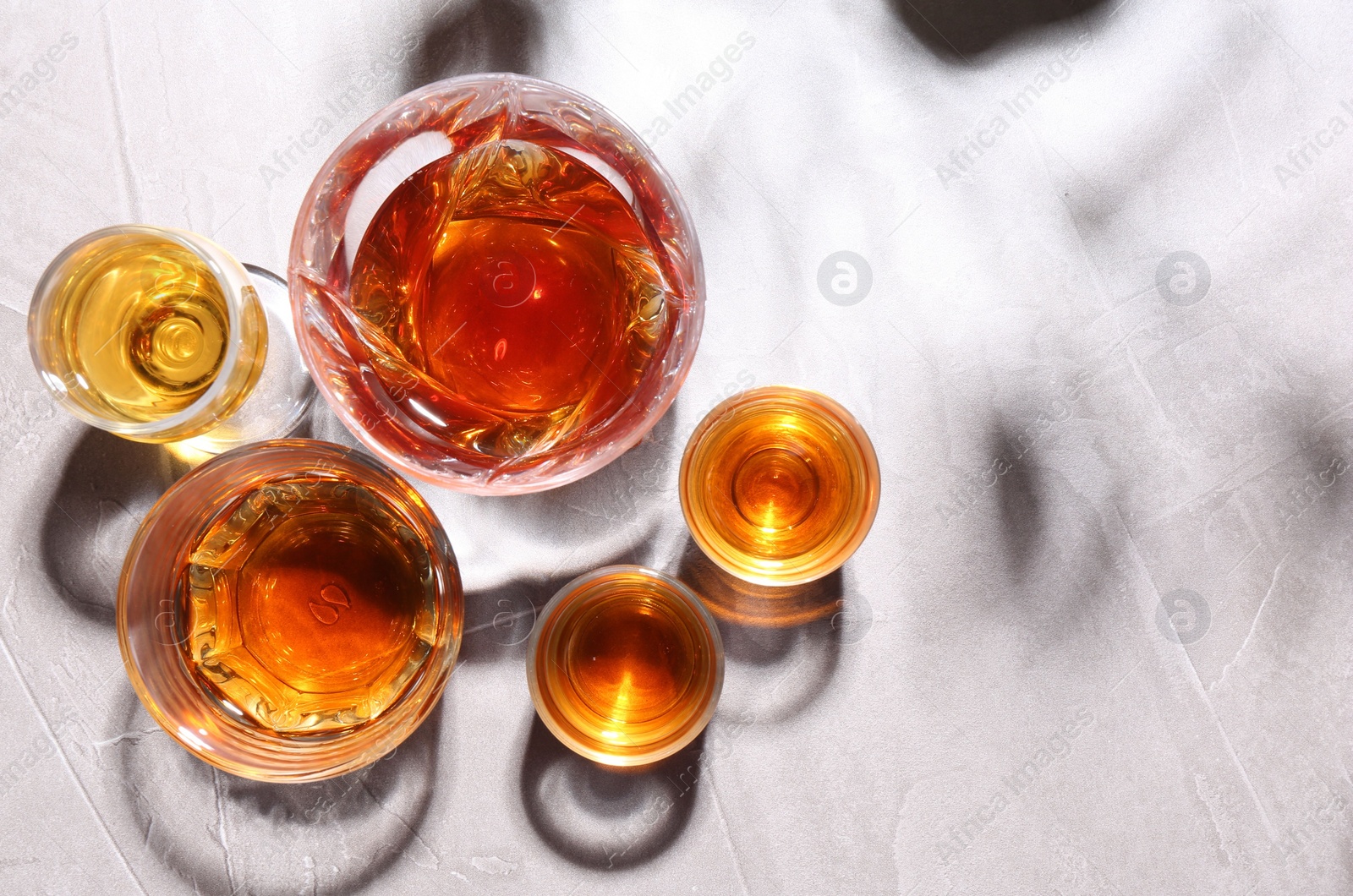 Photo of Many different liqueurs in glasses on light table, flat lay. Space for text