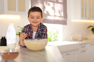 Photo of Cute little boy cooking dough in kitchen at home