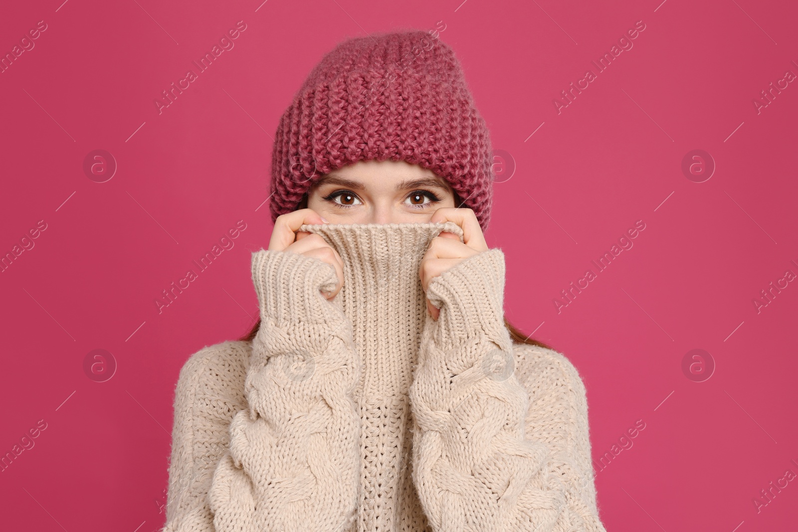 Photo of Young woman wearing warm sweater and hat on crimson background. Winter season