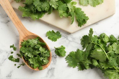 Photo of Fresh green cilantro and wooden spoon on white marble table, flat lay