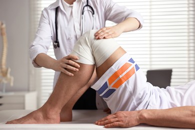 Photo of Sports injury. Doctor examining patient's knee in hospital, closeup