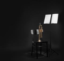 Photo of Trumpet, chair and note stand with music sheets on black background. Space for text