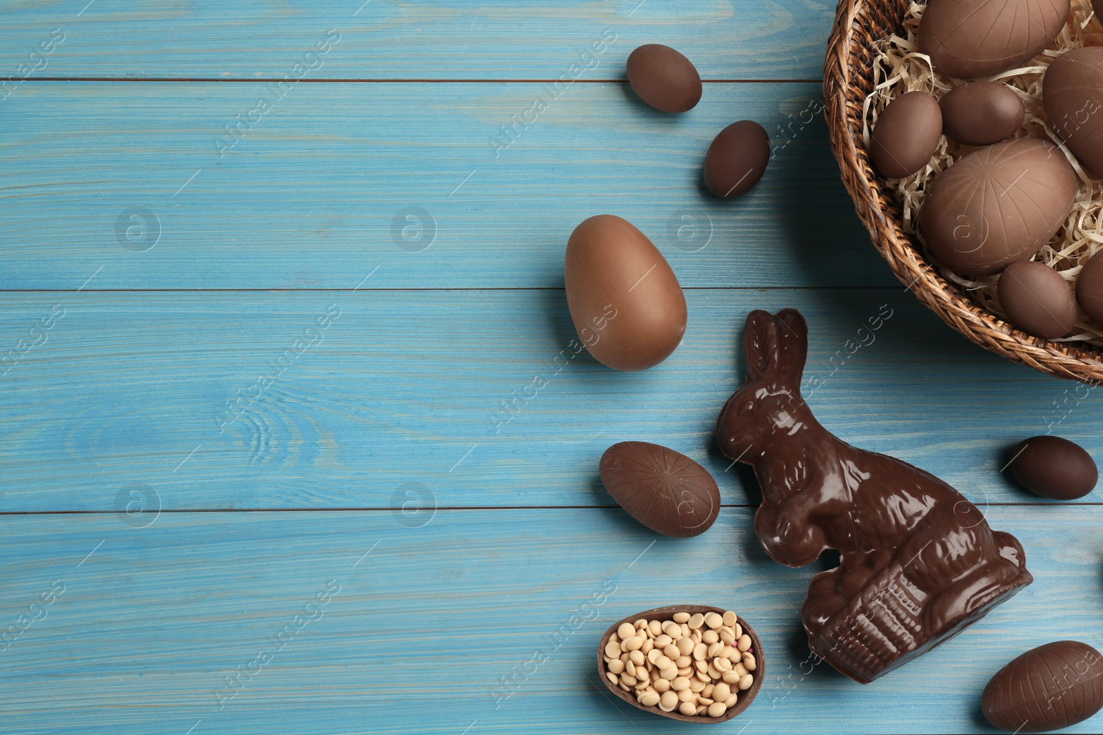 Photo of Chocolate Easter bunny and eggs on light blue wooden table, flat lay. Space for text