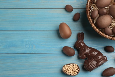 Chocolate Easter bunny and eggs on light blue wooden table, flat lay. Space for text