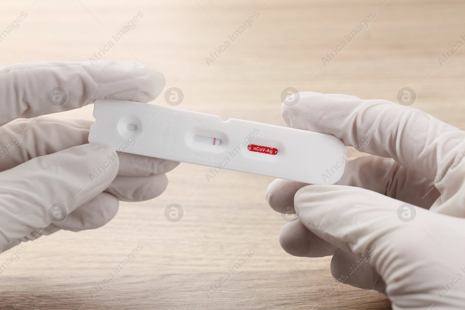 Photo of Doctor holding disposable Covid-19 express test at wooden table, closeup