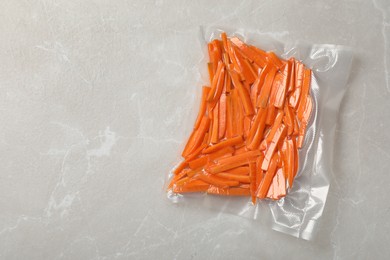 Photo of Vacuum packing with cut carrots on light grey marble table, top view. Space for text