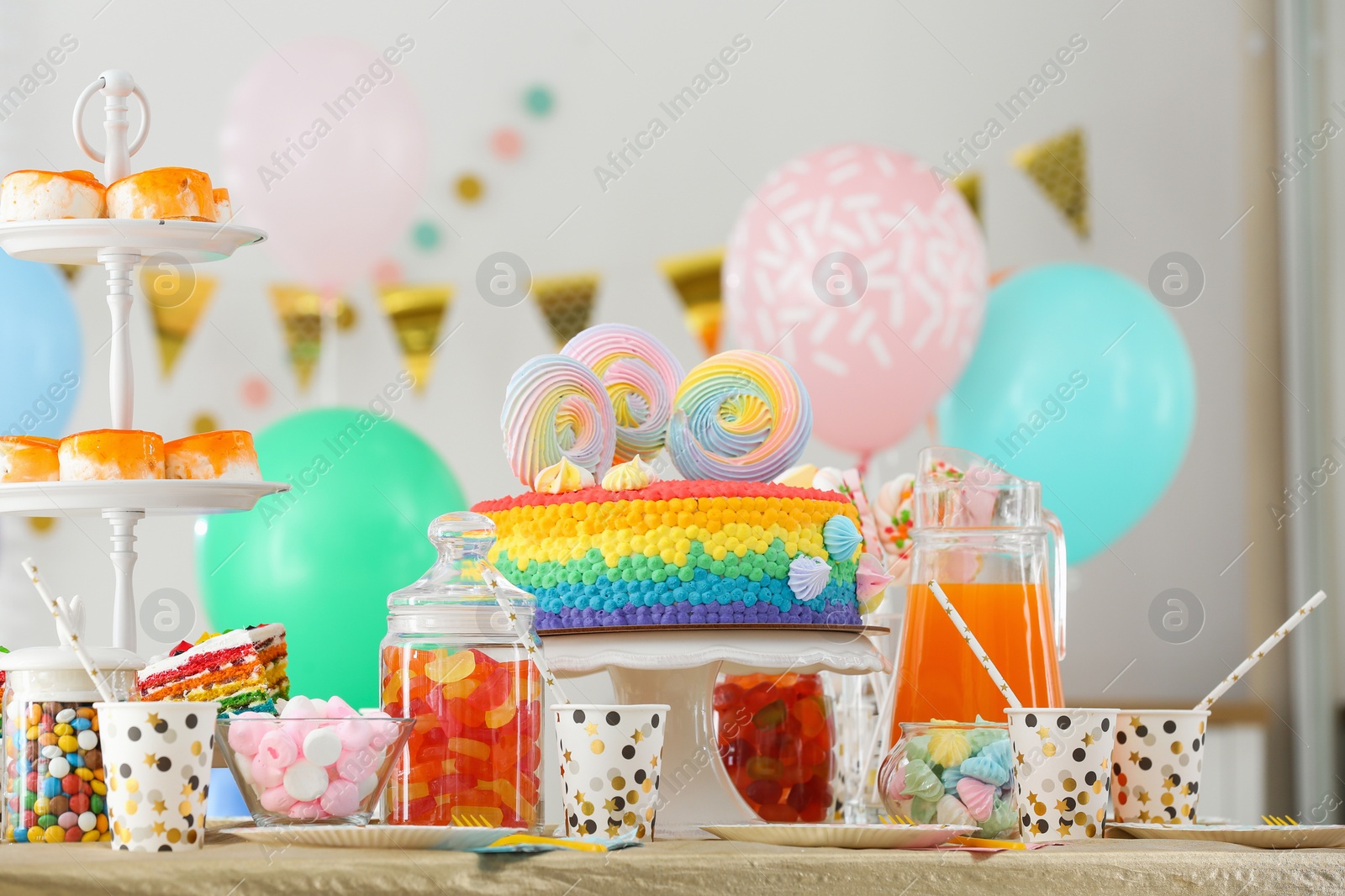 Photo of Bright birthday cake and other treats on table in decorated room