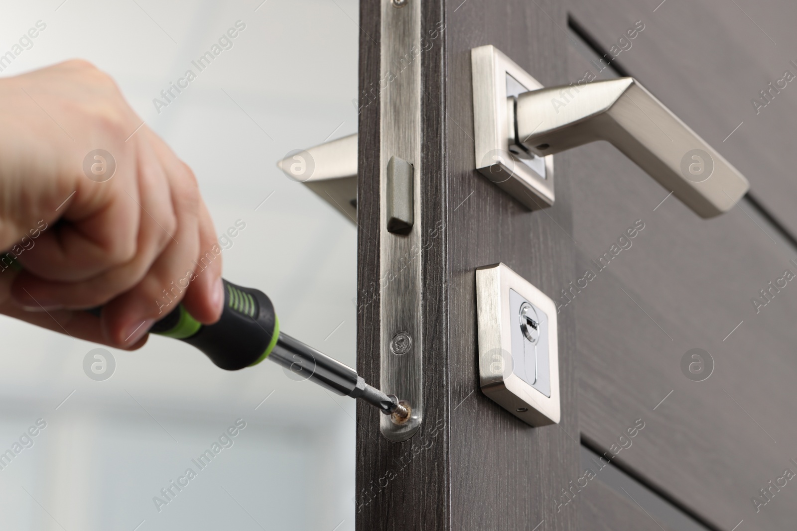 Photo of Handyman with screwdriver repairing door lock indoors, closeup