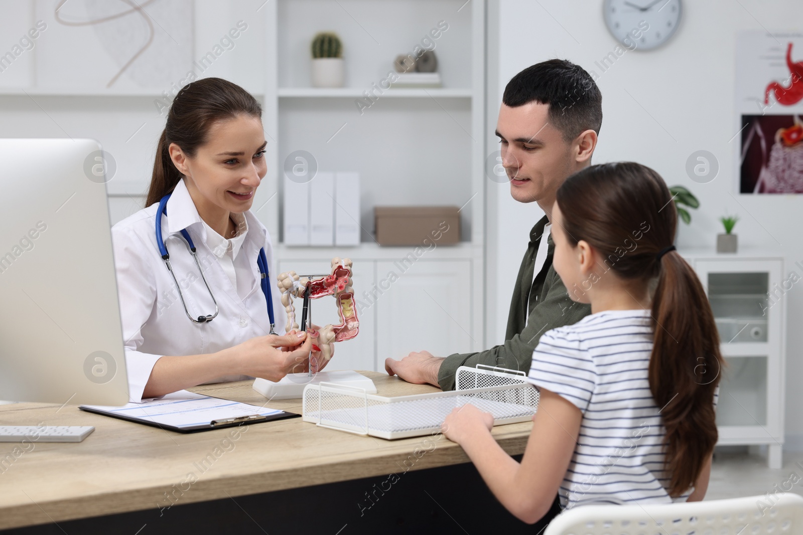 Photo of Gastroenterologist with model of intestine consulting man and his daughter in clinic