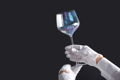 Photo of Person in white gloves checking cleanliness of glass on dark background, closeup. Space for text