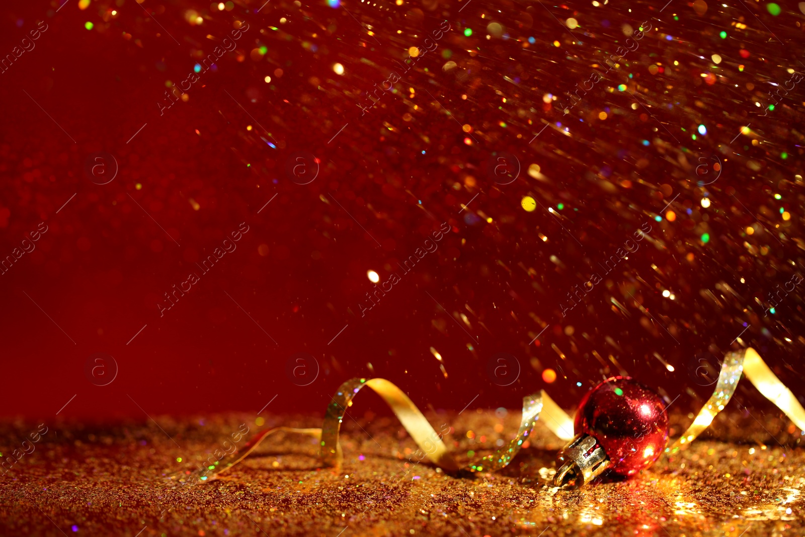 Photo of Golden glitter, Christmas ball and streamer against color background. Space for text
