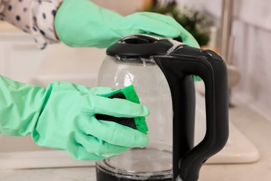 Photo of Woman cleaning electric kettle with sponge at countertop in kitchen, closeup