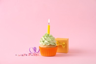 Photo of Birthday cupcake with burning candle and gift box on pink background
