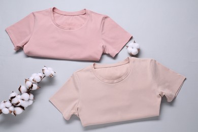 Photo of Cotton branch with fluffy flowers and t-shirts on light gray background, flat lay