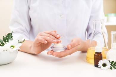 Female dermatologist testing skin care product at table, closeup