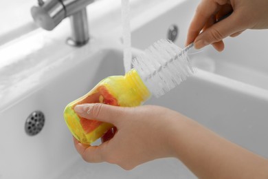 Photo of Woman washing baby bottle with brush in kitchen, closeup