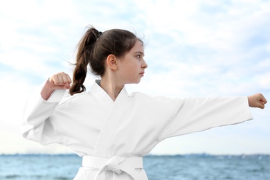 Photo of Cute little girl in kimono practicing karate near river