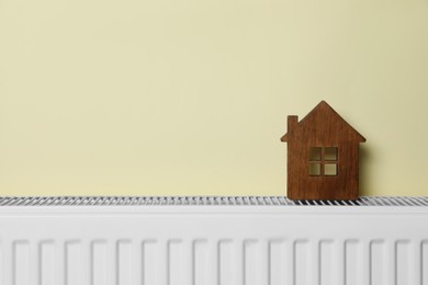 Photo of Wooden house model on heating radiator near beige wall, space for text. Energy efficiency concept