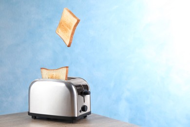 Photo of Bread slices popping up from modern toaster on wooden table. Space for text