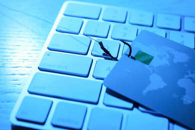 Photo of Fishing hook with credit card and computer keyboard on table, closeup. Cyber crime