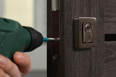 Photo of Handyman with drill repairing door lock indoors, closeup