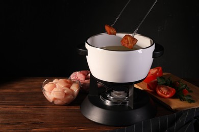 Photo of Dipping pieces of fried meat into oil in fondue pot at wooden table, space for text