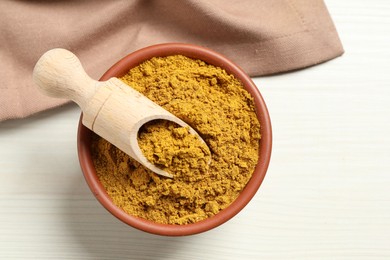 Photo of Curry powder in bowl and scoop on white wooden table, top view