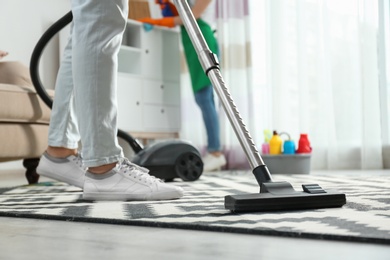Photo of Cleaning service professional vacuuming carpet indoors, closeup
