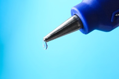 Photo of Dripping hot glue from gun on light blue background, closeup