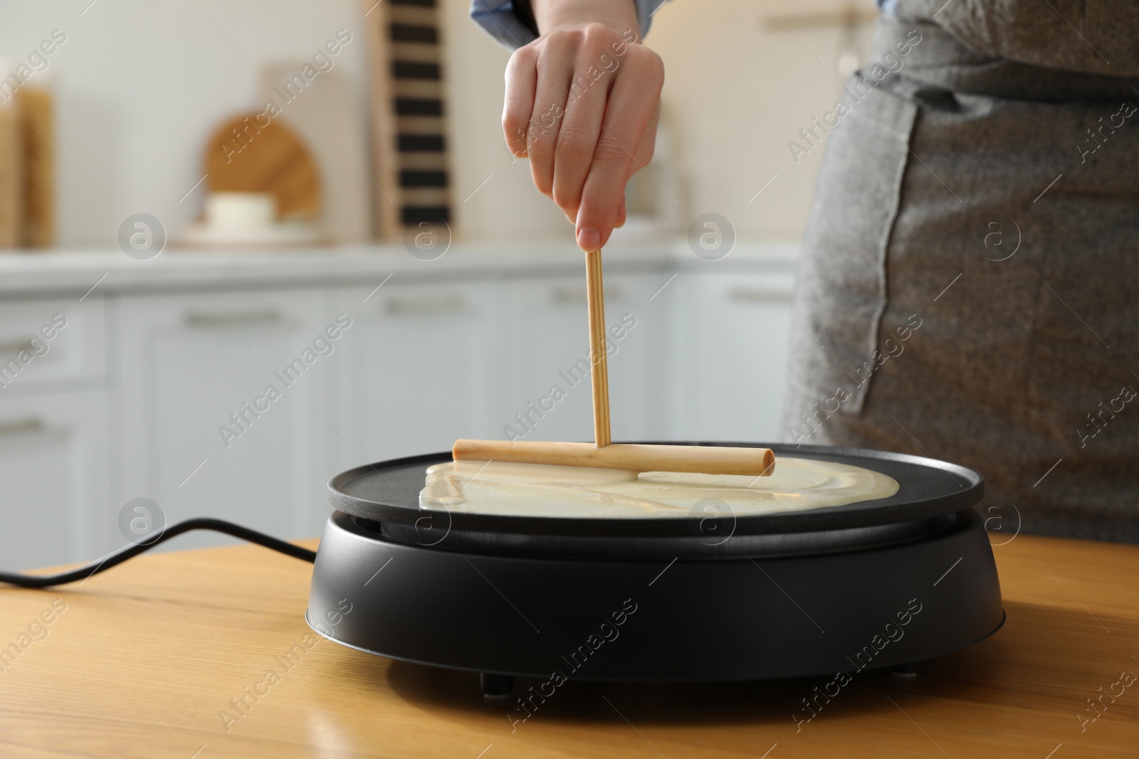 Photo of Woman cooking delicious crepe on electrical pancake maker in kitchen, closeup