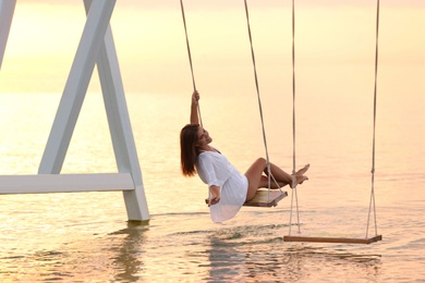 Photo of Young woman enjoying sunrise on swing over water