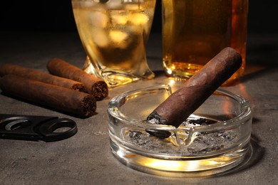 Photo of Cigars, ashtray, whiskey and cutter on grey table, closeup