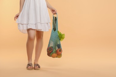 Photo of Woman with string bag of fresh vegetables on beige background, closeup. Space for text