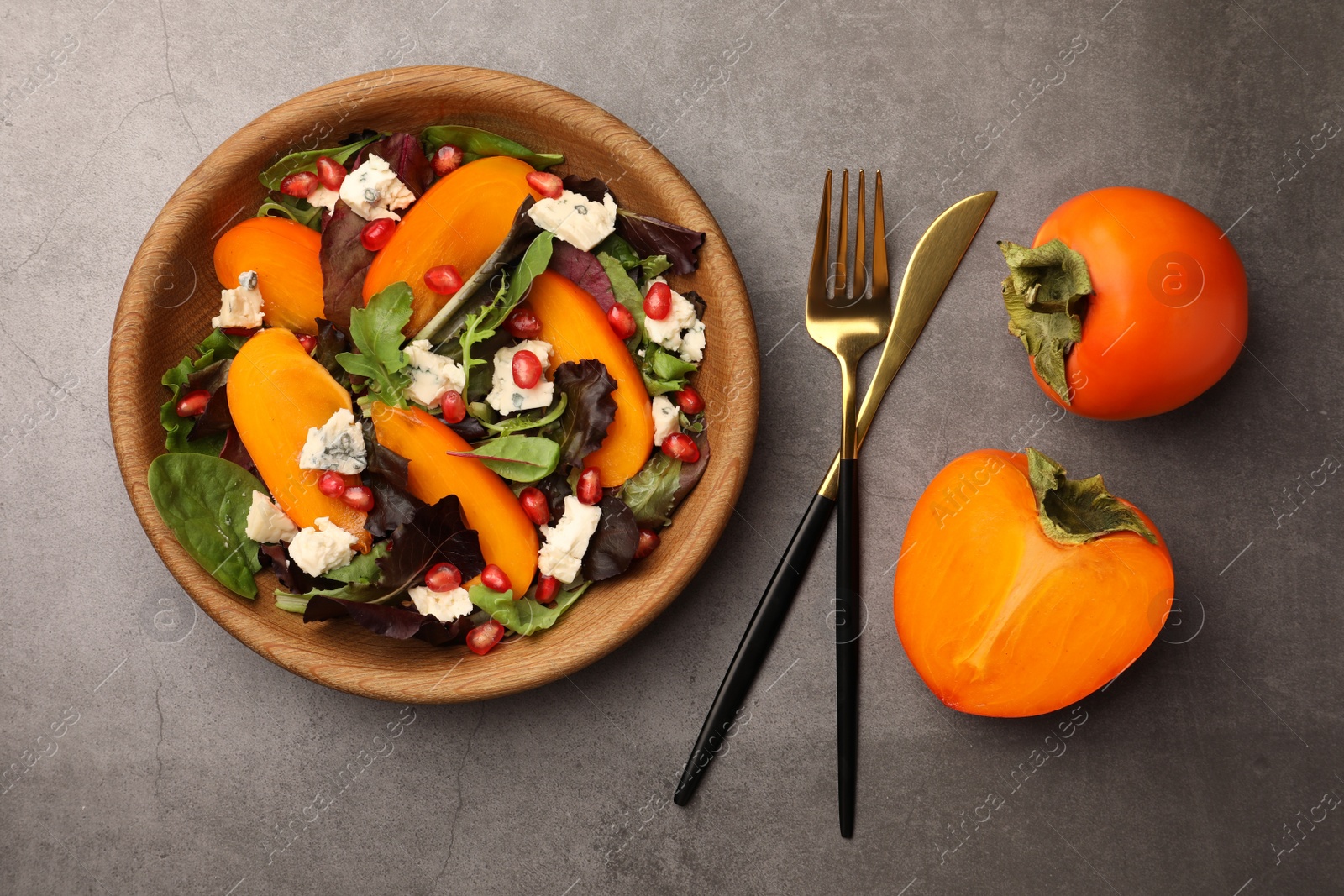 Photo of Delicious persimmon salad with cheese and pomegranate served on grey table, flat lay