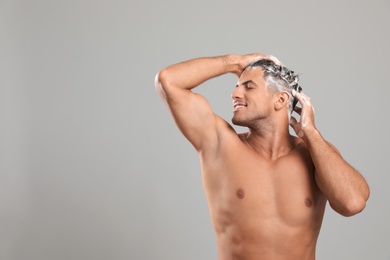 Photo of Handsome man washing hair on grey background, space for text
