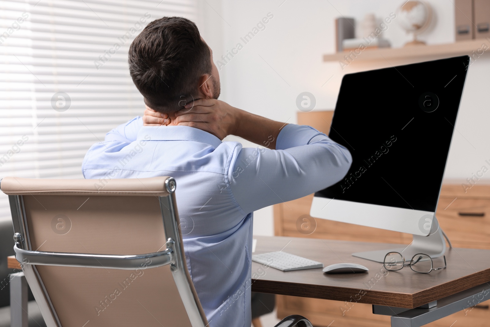 Photo of Man massaging stiff neck in office, back view