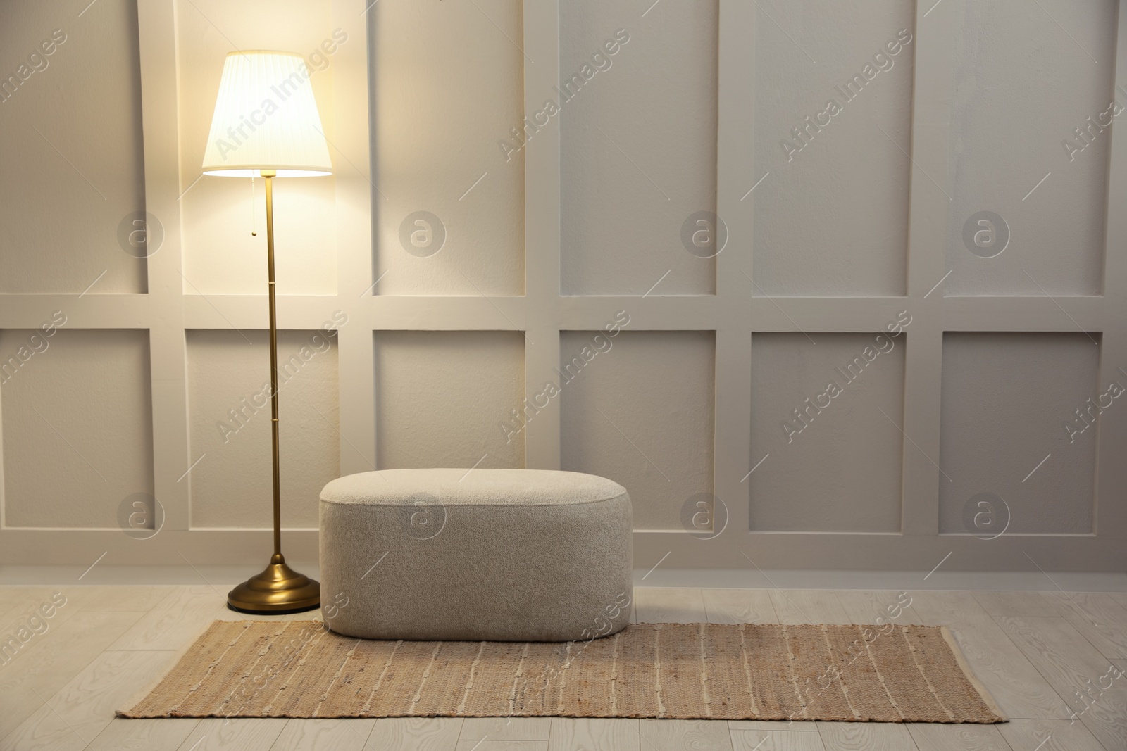 Stylish room interior with beige rug, ottoman and lamp near white wall. Space for text Photo of Stylish room interior with beige rug, ottoman and lamp near white wall. Space for text