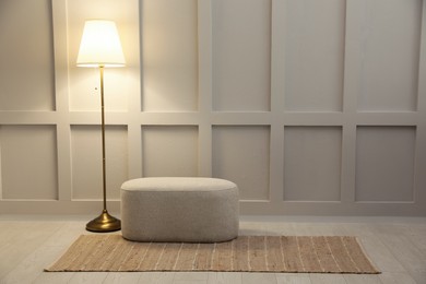 Photo of Stylish room interior with beige rug, ottoman and lamp near white wall. Space for text