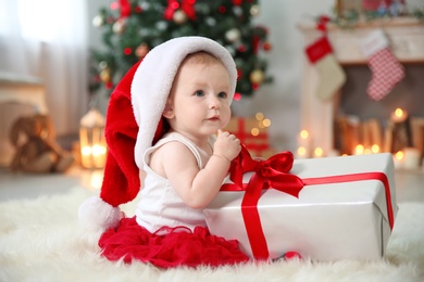 Photo of Cute baby in Santa hat opening gift box at home. Christmas celebration