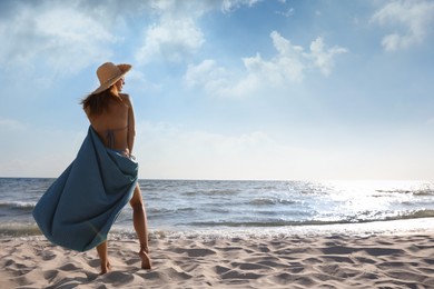 Photo of Woman with beach towel and straw hat on sand near sea, back view. Space for text