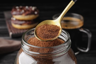 Photo of Spoon of instant coffee over jar on black table, closeup